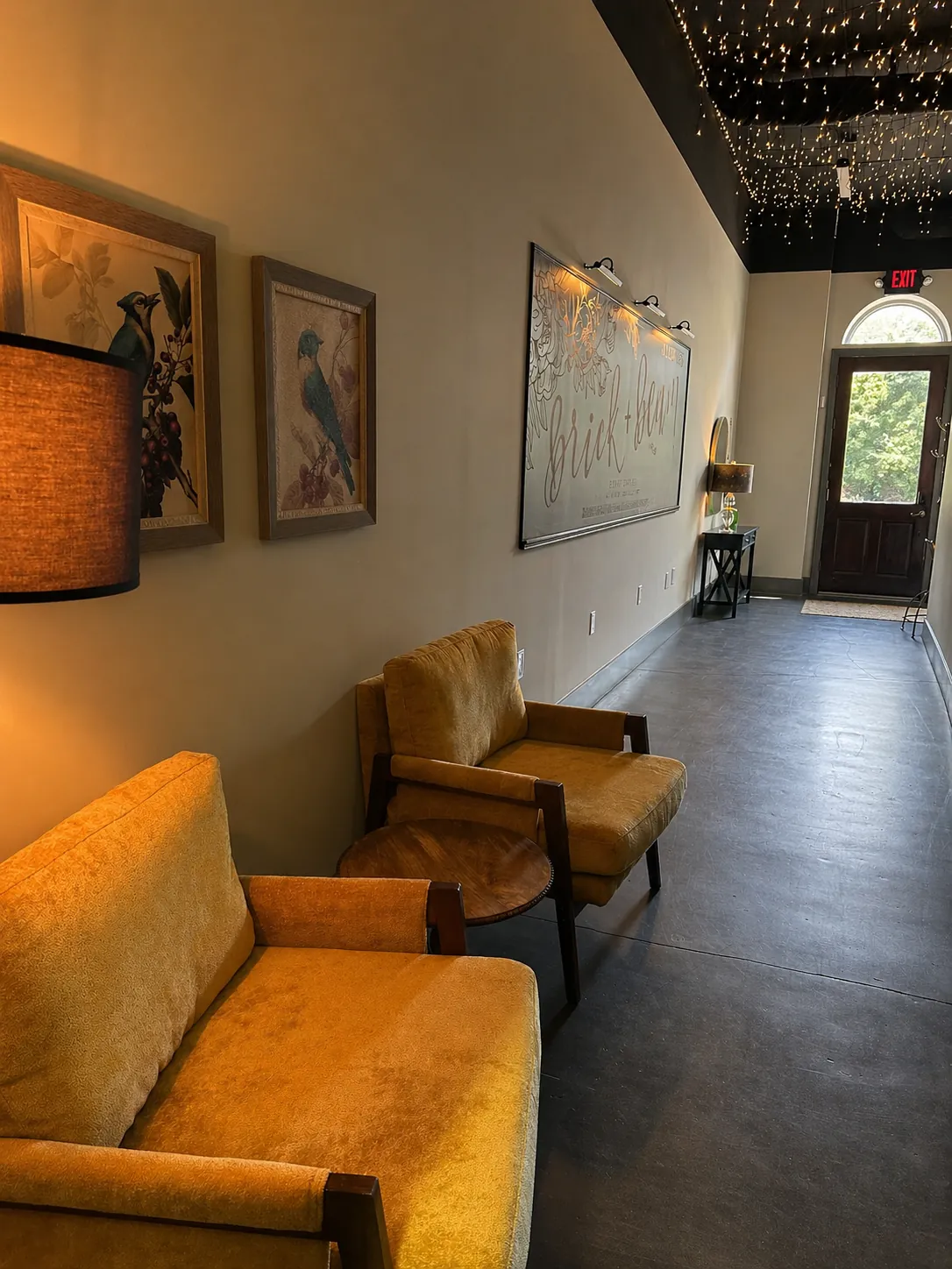 Brick and Beam lounge area with vintage chairs, wall art, string lights, and entry door