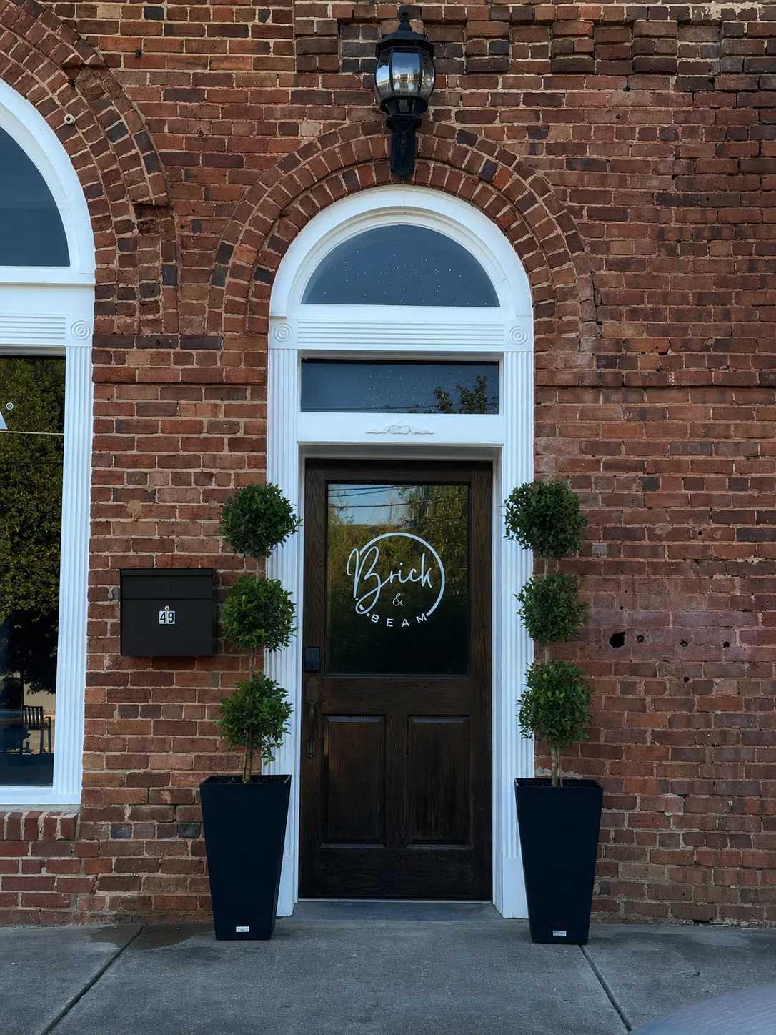 Brick and Beam exterior entrance with brick facade, arched doorway, logo window, and topiary planters