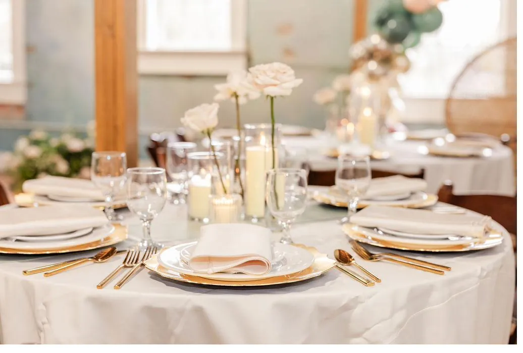 Elegant round table setting at Brick and Beam with white roses, pillar candles, and gold chargers