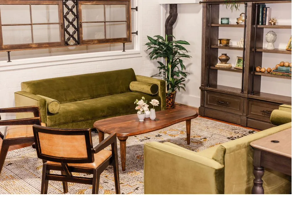 Brick and Beam Events lounge sitting area with olive velvet sofa, wood coffee table, and vintage bookcase